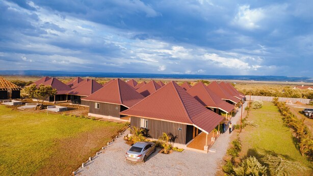 A row of modern, single-story houses with red roofs, arranged in a linear fashion along a gravel driveway. - Captain James Camp (Naivasha)