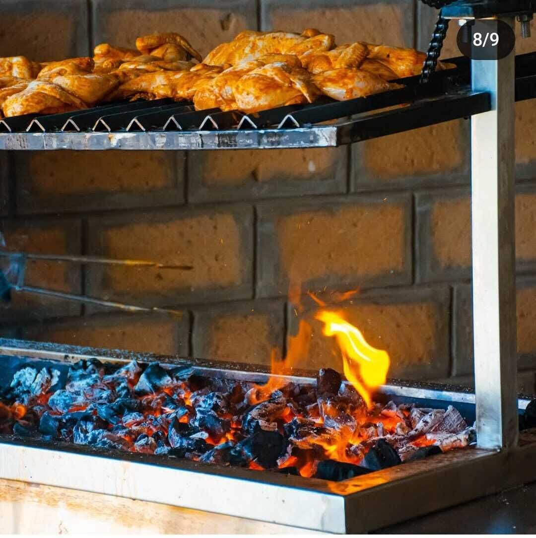 A grill with food being cooked over charcoal, set against a brick wall.