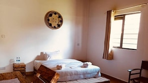 A bedroom with a bed, a wooden table, a chair, a window, and a wall decoration. - Captain James Camp (Naivasha)