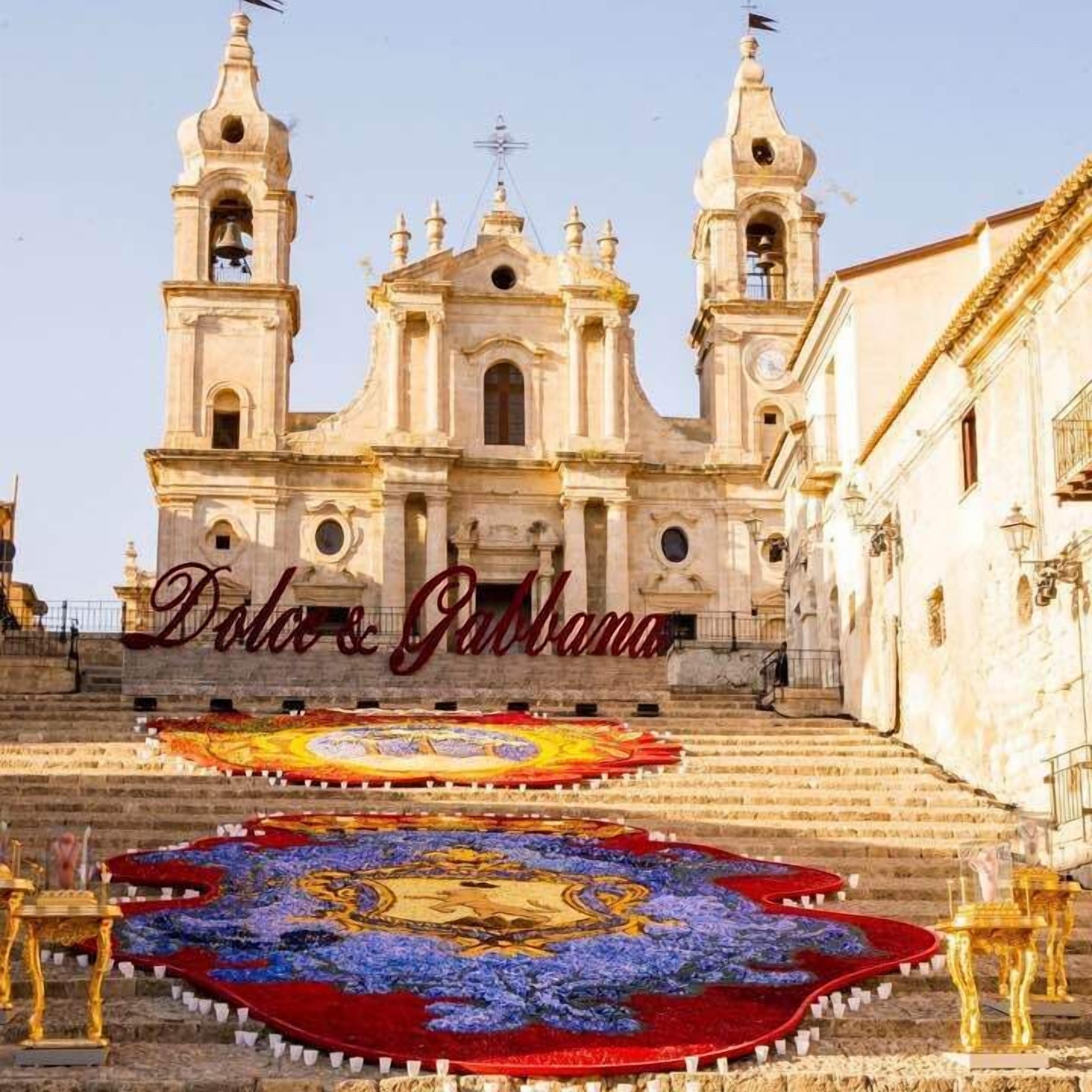 Uma igreja histórica com uma torre de sino e um tapete grande e colorido nos degraus.