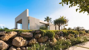 A modern building with a minimalist design, surrounded by a landscaped garden with large rocks and white flowers. - Luxury villa with pool and spa - Dicasainsicilia (Riposto)