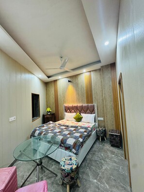 A bedroom with a bed, a glass table, a stool, and a ceiling fan.