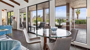 A modern interior with a glass table and chairs, large windows, and a view of greenery and a building. - Ozone Pool, Spa and Built-In Bar (Palm Springs)