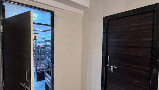 A hallway with a tiled floor, a door with a handle, and a window with a decorative grille. - Aarav Dormitory (Itarsi)