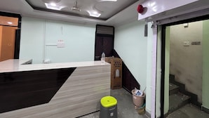 A hotel room with a modern design, featuring a large desk, a small trash bin, and a water bottle on the floor. - Aarav Dormitory (Itarsi)