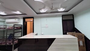 A hotel room with a large bed, a desk, a ceiling fan, and a window. - Aarav Dormitory (Itarsi)