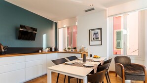 A modern kitchen with a built-in oven, a dining area with a table and chairs, and a large window with shutters. - PORT LYMPIA AP4429 By Riviera Holiday Homes (Niza)