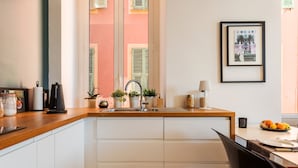 A modern kitchen with a wooden countertop, white cabinets, a sink, and a dining area with a table and chairs. - PORT LYMPIA AP4429 By Riviera Holiday Homes (Niza)