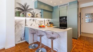 A modern kitchen with a central island, bar stools, and a decorative wall with palm prints. - LE LAFAYETTE AP4410 By Riviera Holiday Homes (Niza)