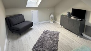 A modern loft bedroom with a skylight, a grey sofa, a grey cabinet with a TV, and a fluffy rug.