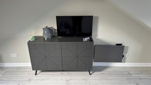 A modern living room with a flat-screen TV on a stand, a decorative vase, and a kettle on a grey cabinet.