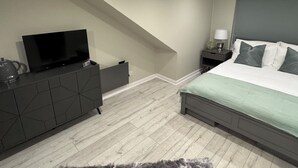 A bedroom with a bed, a TV on a dresser, a nightstand with a lamp, and a staircase.