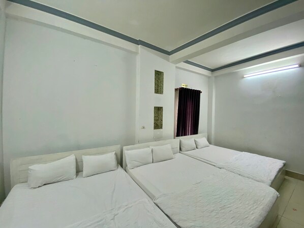 A hotel room with two beds, a window with a curtain, and a ceiling light.