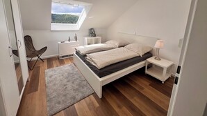 A bedroom with a skylight, a bed, a chair, a nightstand, and a lamp. - Tannenherz vacation apartment with balcony and mountain view (Winterberg)