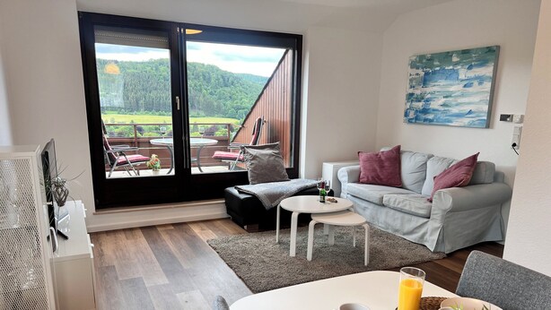 A modern living room with a large sliding glass door leading to an outdoor patio. - Tannenherz vacation apartment with balcony and mountain view (Winterberg)