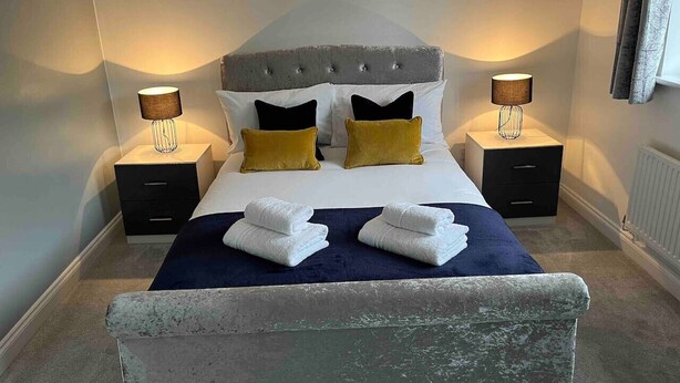 A neatly made bed with a grey upholstered headboard, two bedside tables with lamps, and a blue throw blanket.