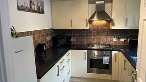 A compact kitchen with white cabinets, a black countertop, a stainless steel stove, and a microwave.