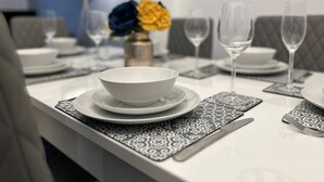 A dining table set with plates, bowls, and glasses, with a vase of flowers in the background.