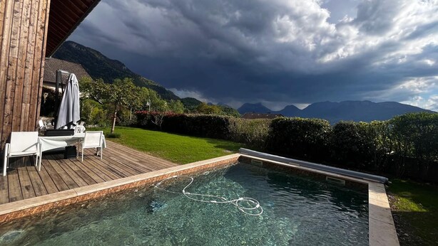 Una piscina con agua cristalina, rodeada por una terraza de madera y sillas reclinables blancas.