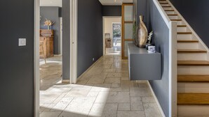 Un pasillo moderno con una escalera, una consola decorada con objetos y vista a otra habitación.