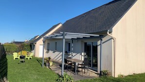 Une maison dotée d’un patio couvert, d’une pelouse et d’un petit jardin.