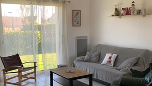 Un salon comprenant un canapé, un fauteuil, une table basse et une porte-fenêtre coulissante donnant sur un balcon.