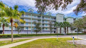Un hotel de varios pisos con balcones, palmeras y un césped bien cuidado.