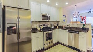 Una cocina moderna con gabinetes blancos, electrodomésticos de acero inoxidable, microondas, horno y lavavajillas.