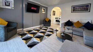 Un salon moderne avec un canapé gris, une table basse et un tapis à motifs. Un téléviseur à écran plat est fixé au mur.