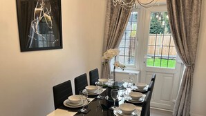 Une salle à manger avec une table noire dressée pour six personnes, des chaises blanches et un lustre.