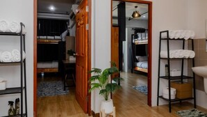 A compact hotel room with a wooden floor, a bed, a small desk, a potted plant, and a shelf with towels. - 22 Hostel (Chiang Mai)