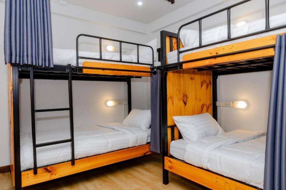 A room with two bunk beds, each with a wooden frame and white bedding. There are two bedside tables with lamps, and the room has a wooden floor.