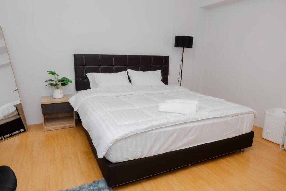 A neatly made bed with white bedding in a modern room with a wooden floor and a black headboard.