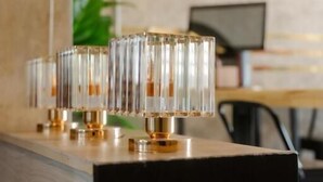 A modern interior with a wooden counter and a series of clear, cylindrical glass lamps with gold bases. - 22 Hostel (Chiang Mai)