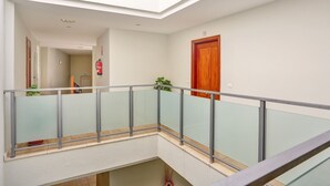 Un interior amb diversos nivells, una barana de vidre, una porta de fusta i un extintor fixat a la paret.