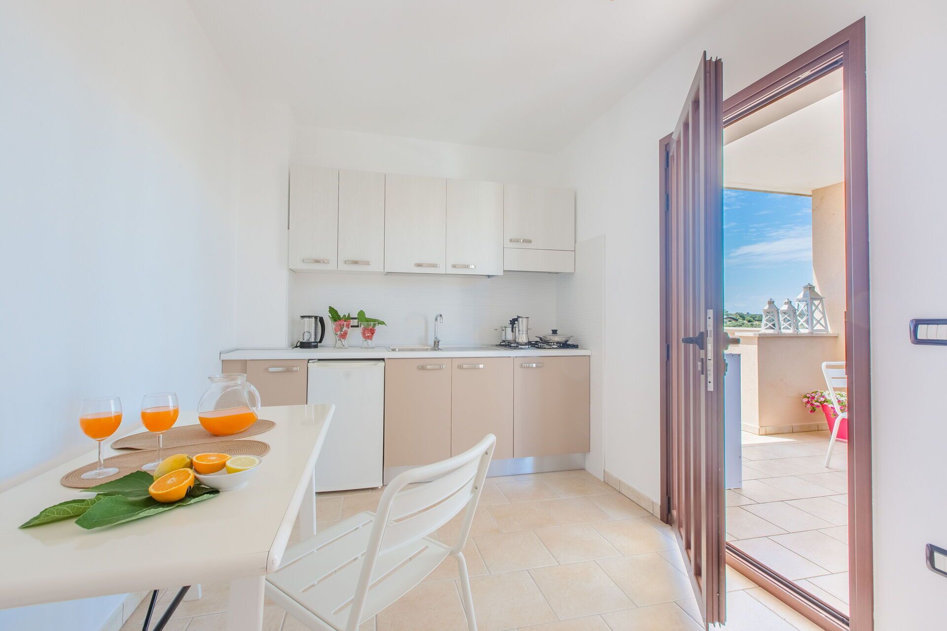 A compact kitchen with white cabinets, a dining table with chairs, and a view of the outdoors through an open door.