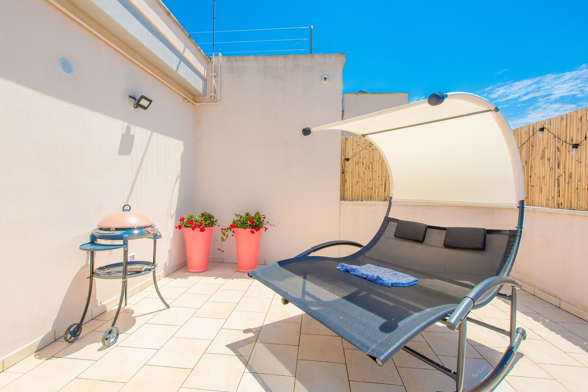 A patio with a metal chair, a small table, and two potted plants.