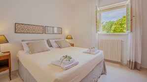 Un dormitorio con una cama grande, dos mesitas de noche, una ventana con cortinas y un radiador.