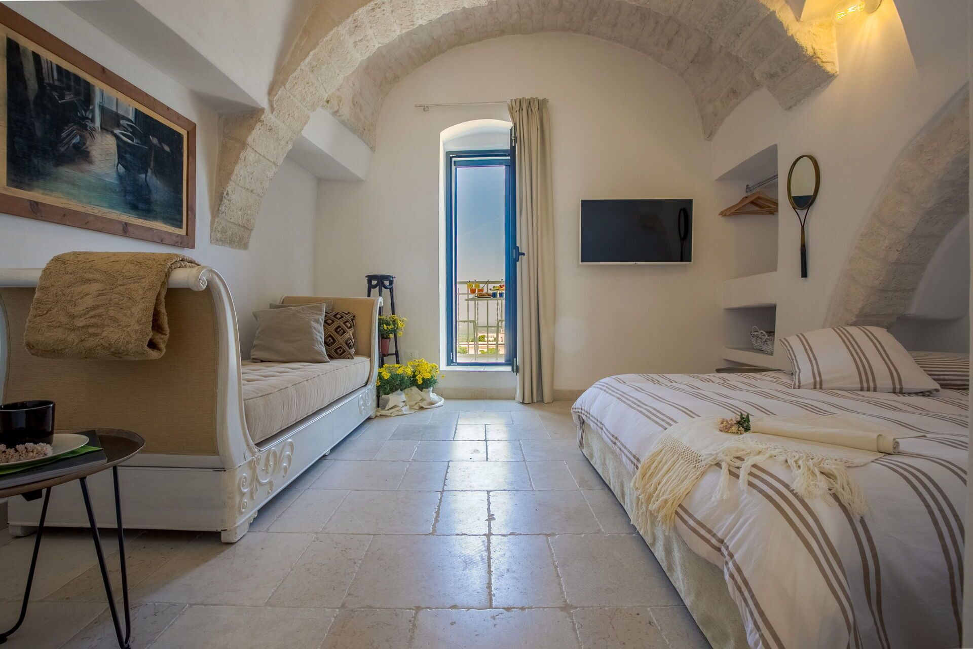 A cozy bedroom with a sofa, a bed, a TV, and a balcony with a view.