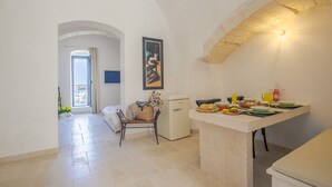 Una cocina moderna con comedor, que presenta un arco de piedra, un refrigerador pequeño y una mesa para desayunar con platos, vasos y un frutero.