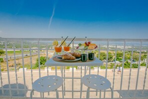 Un balcón con una mesa preparada para el desayuno, que incluye croissants, fruta y bebidas, con vistas a un paisaje pintoresco.