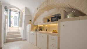 Una cocina estrecha con armarios blancos, un microondas y una tetera sobre la encimera.