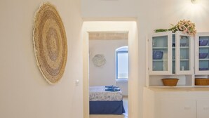 Un couloir orné d’une tapisserie murale tissée, un lit recouvert d’une courtepointe bleue et un meuble avec des portes en verre contenant de l’ustensile de cuisine.