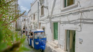 Une rue étroite bordée d’immeubles blancs, un véhicule bleu à trois roues et une porte verte.