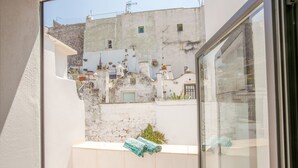 Une vue depuis un balcon avec un mur blanc et une fenêtre, donnant sur une rue étroite bordée d’immeubles et agrémentée d’un cactus.