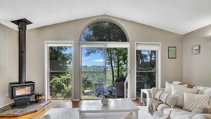 A cozy living room with a fireplace, a white sofa, a coffee table, and large windows offering a view of the outdoors.