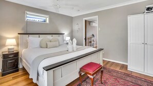 A bedroom with a bed, bedside tables, a ceiling fan, a window, a wardrobe, and a red bench.