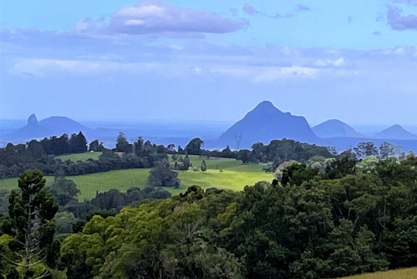 A landscape with rolling hills, dense forests, and distant mountains under a clear sky.