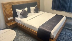 Ein ordentlich bezogenes Bett mit Holz-Kopfteil, zwei Kissen und einer dunklen Tagesdecke.