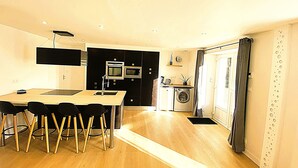 A compact kitchen with modern appliances, a dining area with a table and chairs, and a laundry machine. - L'instant d'un souvenir Gite 10 people 135 m² - 4 bedrooms - 7 beds - 2 bathrooms (Taupont)